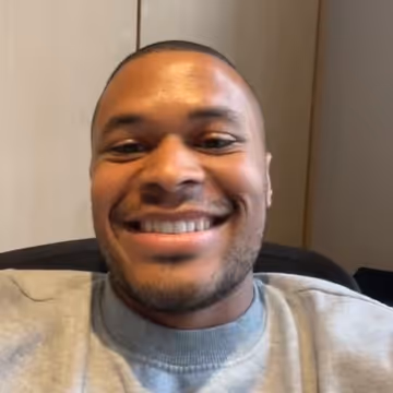 Un homme souriant aux cheveux courts, portant un sweat-shirt gris, se trouve à l'intérieur.